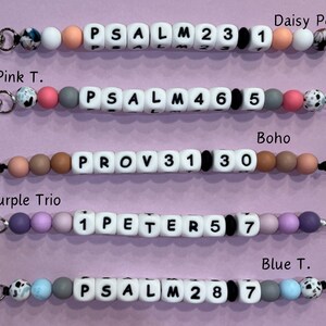 May include: Five colorful beaded keychains with different bible verses and numbers. Each keychain has a silver clasp and a black string.