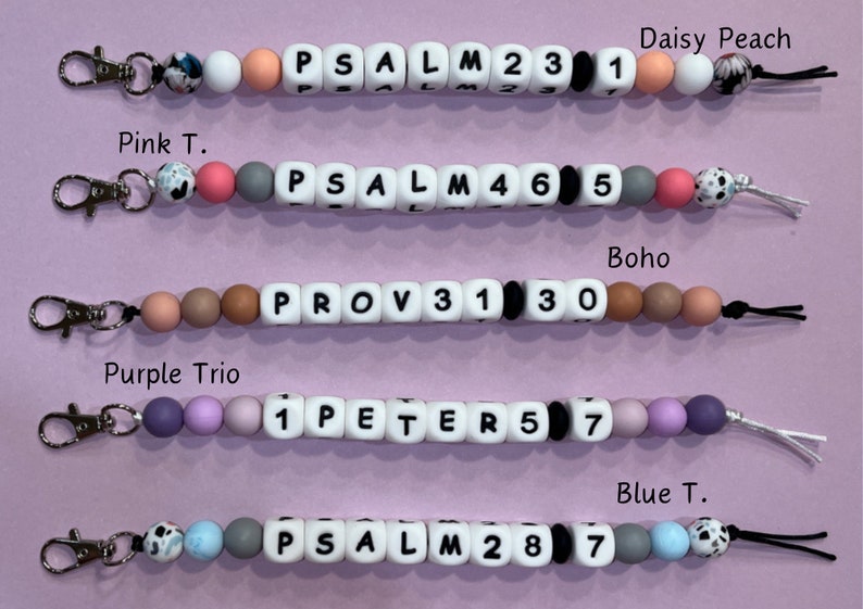 May include: Five colorful beaded keychains with different bible verses and numbers. Each keychain has a silver clasp and a black string.