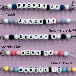 May include: Five colorful silicone bead keychains with different names and numbers. The keychains are in the following colors: daisy blue, light pastel, speckle black/white, speckle pink, and flower power.