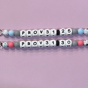 May include: Two beaded keychains with silver clasps. The top keychain has blue and white beads with the text "PROV 31 1 25". The bottom keychain has pink and white beads with the text "PROV 31 1 30".