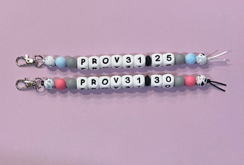 May include: Two beaded keychains with silver clasps. The top keychain has blue and white beads with the text "PROV 31 1 25". The bottom keychain has pink and white beads with the text "PROV 31 1 30".