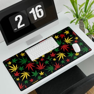 May include: A black desk mat with a repeating pattern of green, yellow, and red marijuana leaves. The mat is designed for use with a computer keyboard and mouse.