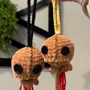 Può includere: Due ornamenti a forma di medusa all'uncinetto fatti a mano. Ognuno ha un corpo marrone con occhi a bottone neri e tentacoli con frange rosse. Uno ha un cordino nero, l'altro un cordino giallo. Le meduse sono morbide e soffici.
