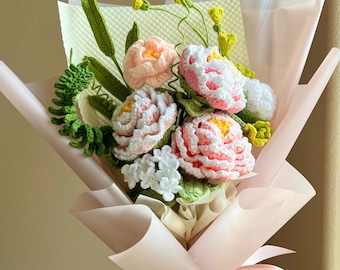 Puede incluir: Un ramo de flores de ganchillo con peonías rosas y blancas, pequeñas flores blancas y follaje verde similar a un helecho. El arreglo está envuelto en papel rosa claro con una cinta a juego e incluye el texto Bestjellyfish en la base.