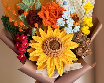 May include: A crochet flower bouquet featuring a large yellow sunflower, an orange rose, small blue flowers, red blossoms, and green leaves. The arrangement is wrapped in brown paper with a brown ribbon and the text Bestjellyfish printed on it.