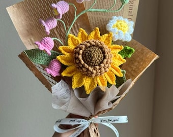 May include: A crocheted bouquet of flowers in a brown paper wrapper. The bouquet includes a yellow sunflower, pink bell-shaped flowers, and a white daisy. The bouquet is tied with a white ribbon with the text "Just for you".
