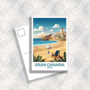 May include: A postcard depicting a beach scene with the text "GRAN CANARIA SPAIN." The illustration shows a sandy beach, blue ocean, and a town with white buildings. A blue beach chair and a small table with an umbrella are on the beach.