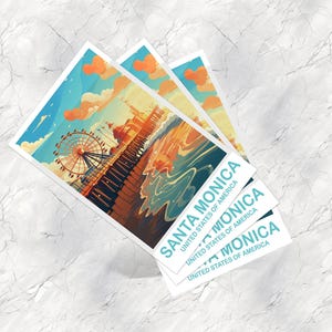 Op de afbeelding: Drie Santa Monica kunstafdrukken. Elke afdruk toont een kleurrijke illustratie van de Santa Monica Pier met een reuzenrad, oceaan en lucht. De afdrukken hebben de tekst "SANTA MONICA" en "UNITED STATES OF AMERICA".