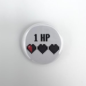 Pode incluir: Uma caneca de cerâmica branca com uma alça preta e o texto "But First, Coffee" em preto, em negrito. A caneca está sobre uma superfície branca.