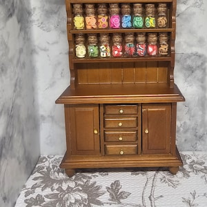 May include: A miniature wooden hutch with a display shelf holding small glass jars filled with colorful fruit-shaped polymer clay. The hutch has two doors, three drawers, and a dark brown finish.