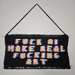 Peut inclure: Suspension murale en crochet noir avec le texte "FUCK OFF MAKE REAL FUCKING ART" en couleurs arc-en-ciel. L'œuvre d'art est suspendue par un cordon noir et des chevilles en bois.