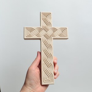 Könnte beinhalten: Ein Holzkreuz mit einem keltischen Knotendesign. Das Kreuz ist hellbraun und hat eine glatte Oberfläche.