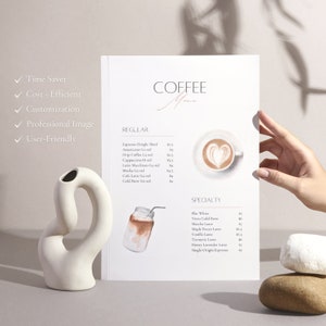 May include: A white coffee menu with a watercolor illustration of a coffee cup and a mason jar with a straw. The menu lists regular and specialty coffee drinks with prices. The text on the menu reads "Coffee Menu", "Regular", "Espresso Single Shot", "Americano (12 oz)", "Drip Coffee (12 oz)", "Cappuccino (8 oz)", "Latte Macchiato (12 oz)", "Mocha (12 oz)", "Cafe Latte (12 oz)", "Cold Brew (16 oz)", "Specialty", "Flat White", "Nitro Cold Brew", "Matcha Latte", "Maple Pecan Latte", "Vanilla Latte", "Turmeric Latte", "Honey Lavender Latte", "Single-Origin Espresso".