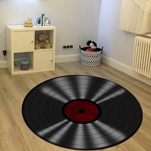 May include: A black and red vinyl record rug with a circular design. The rug is on a wooden floor.