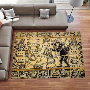 Op de afbeelding: Een rechthoekig vloerkleed met een gele achtergrond en zwarte lijntekeningen van figuren in oude Maya-stijl en hiërogliefensymbolen. Het ontwerp toont twee interagerende figuren, omringd door decoratieve randen met patronen.