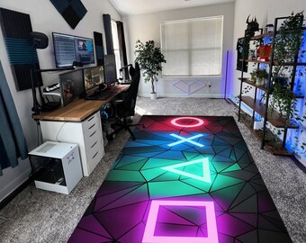 Puede incluir: Una alfombra rectangular con un fondo geométrico negro de estilo low-poly y un degradado en tonos azules, verdes y morados. La alfombra muestra los cuatro símbolos icónicos del mando de PlayStation: un círculo rojo, una cruz azul, un triángulo verde y un cuadrado rosa.