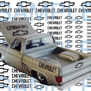 Può includere: Un pick-up Chevrolet argento e beige con il portellone posteriore abbassato. Il camion ha un logo Chevrolet nero sul lato e un logo Chevrolet nero sul portellone posteriore.