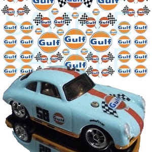 Könnte beinhalten: Ein blaues Spielzeugauto mit einem roten Streifen und einem Gulf-Logo auf der Motorhaube. Das Auto hat ein Schachbrettmuster auf der Motorhaube und die Nummer 58 an der Seite. Das Auto ist von vielen Gulf-Logos und Schachbrettflaggen umgeben.