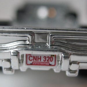 May include: A silver toy car with a red license plate that reads "CNH 320" and the words "NEW JERSEY" in smaller font.