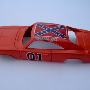 May include: A red toy car model of the General Lee, a 1969 Dodge Charger from the TV show The Dukes of Hazzard. The car has a Confederate flag on the roof and the number 01 on the side.