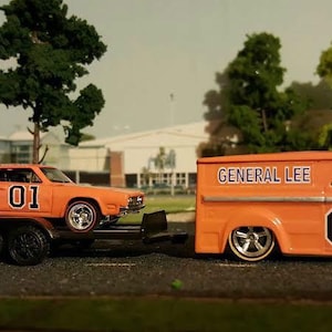May include: A bright orange toy car hauler with the words "General Lee" and the number "01" on the side is hauling a bright orange toy Dodge Charger with the number "01" on the side.