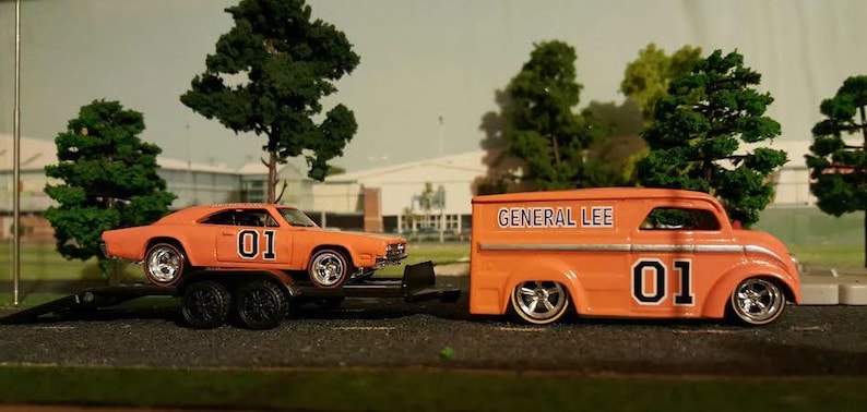 May include: A bright orange toy car hauler with the words "General Lee" and the number "01" on the side is hauling a bright orange toy Dodge Charger with the number "01" on the side.