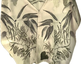 May include: A white silk scarf with a botanical print of leaves and branches in shades of green. The scarf is draped over a hanger.
