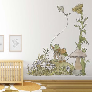 May include: Two green frogs wearing brown clothing are holding a kite string and flying a kite. The frogs are standing on a mushroom with a green and brown background. There are flowers and plants in the background.