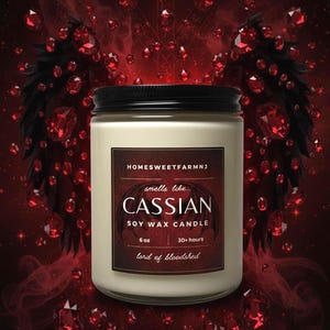May include: A 6 oz soy wax candle in a clear glass jar with a black lid. The label reads: HOMESWEETFARMNJ, smells like... CASSIAN, SOY WAX CANDLE, 6 oz, 30+ hours, lord of bloodshed. The background features dark red wings and floating red gemstones.