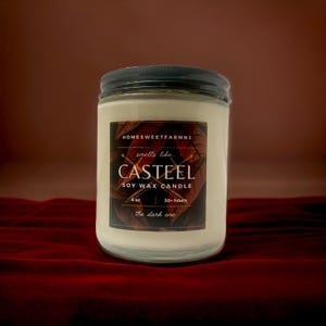 May include: A 6 oz soy wax candle in a clear glass jar with a black lid. The label is brown with gold accents and reads "Homesweetfarmnj smells like... Casteel Soy Wax Candle 6 oz 30+ hours the dark one".