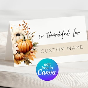 May include: A folded card with a fall theme, featuring pumpkins, flowers, and the text "so thankful for CUSTOM NAME." The design includes a beige stripe and a Canva logo.