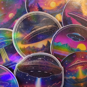 May include: A set of holographic stickers featuring colorful, psychedelic designs of UFOs flying over landscapes. The stickers have a rainbow iridescent finish.