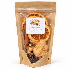 Könnte beinhalten: Ein brauner Papierbeutel mit getrockneten Orangenscheiben, Apfelscheiben, Zimtstangen und ganzen Nelken. Das weiße Etikett trägt die Aufschrift Orion Wellness, Autumn Spice Simmer Pot, APPLE CINNAMON CLOVE ORANGE mit Illustration.