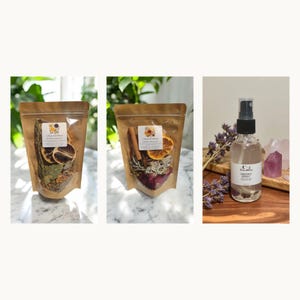 May include: Two stand-up pouches with clear windows containing dried botanicals, including orange slices, cinnamon sticks, and herbs, alongside a clear glass spray bottle labeled Smudge Spray with a black pump top and visible crystals inside.
