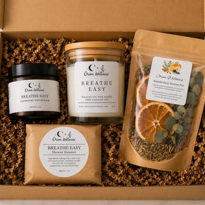 May include: A gift box with self-care items. It contains a jar candle, respiratory support balm, shower steamer, and a simmer pot with dried orange slices. The products are labelled with the text "Breathe Easy" and the brand name "Orion Wellness".