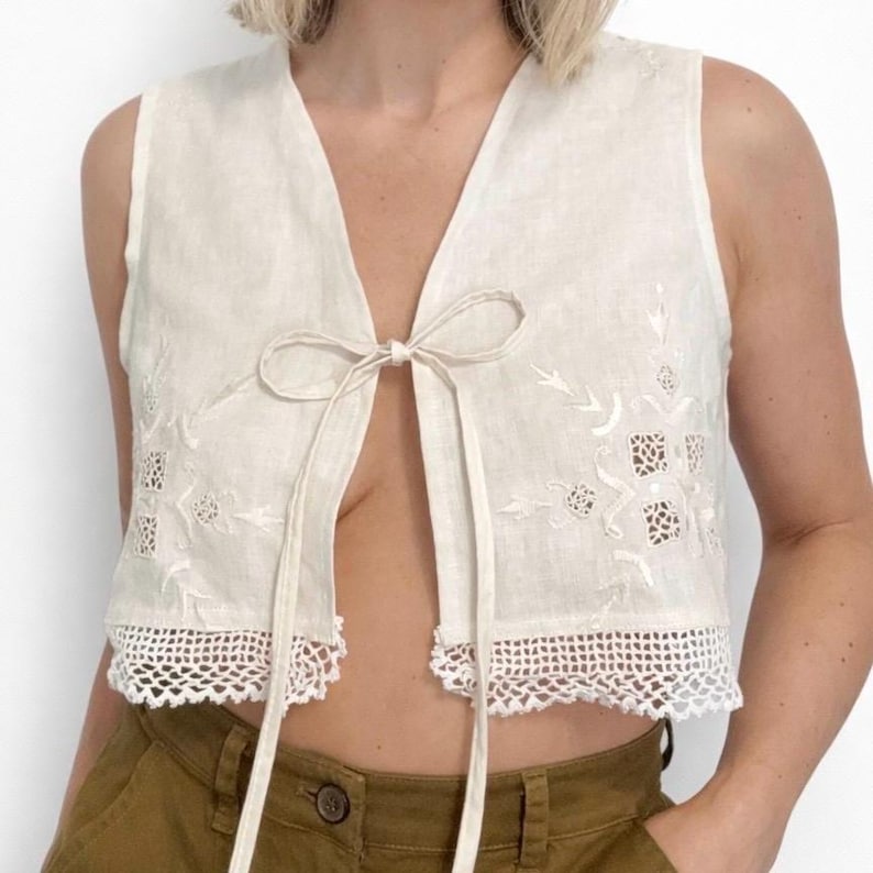 Pu&ograve; includere: Gilet in lino color crema con ricami floreali e rifiniture in pizzo. Il top senza maniche ha una chiusura con fiocco sul davanti. Un capo leggero e traspirante.