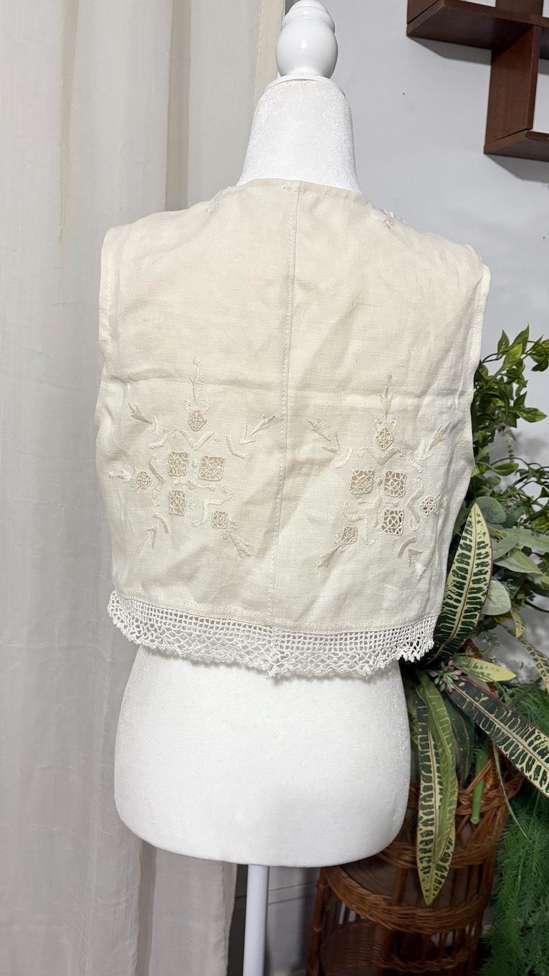 Pu&ograve; includere: Gilet color crema con ricami floreali e un delicato bordo in pizzo. Il gilet &egrave; esposto su un manichino, mettendo in risalto i suoi dettagli intricati e l'estetica vintage. Un capo senza tempo.
