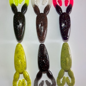 May include: Six soft plastic fishing lures in various colors. The lures have a two-part tail and a body with a speckled design. Colors include black with yellow tips, brown with white tips, and purple with red tips.
