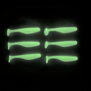 May include: Five glow-in-the-dark fishing lures, each shaped like a slender fish with a pointed tail. The lures are arranged in a row, with the tails pointing in opposite directions.