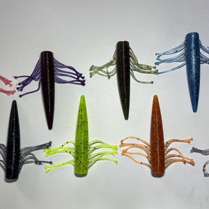 May include: An assortment of eight soft plastic fishing lures in various colors, including red, purple, black, green, blue, and orange. Each lure has a tapered body and multiple tentacle-like appendages, designed to mimic aquatic prey.