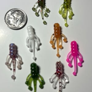 May include: Assortment of eight small, colorful, soft plastic fishing lures. Each lure has a segmented body and multiple tentacles. The lures are in various colors, including green, white, pink, orange, and purple.