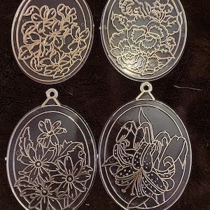 May include: Four black oval-shaped ornaments with gold floral designs. Each ornament features a different floral pattern, including lilies, roses, and daisies.