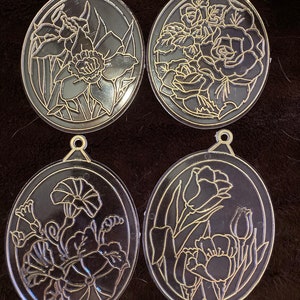 May include: Four black and gold oval ornaments with different floral designs. Each ornament has a gold loop at the top for hanging.