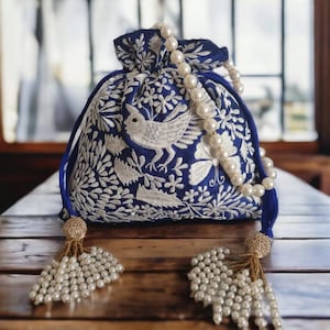 May include: A blue drawstring bag with white embroidery of a bird and floral designs. The bag has a pearl strap and pearl tassels.