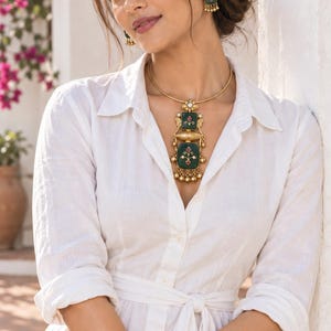 May include: A gold-toned necklace and matching earrings set featuring square, dark green enamel pendants with small floral motifs, pink accents, and dangling gold beads. The necklace is worn on a thin, rigid gold-toned collar band.