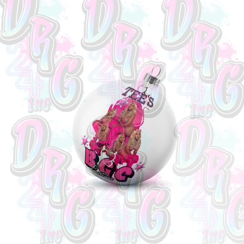 May include: White Christmas ornament with a pink and white design featuring a woman and the text "Tee's Big Edition".