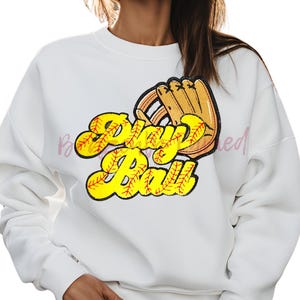 May include: White sweatshirt with a yellow and red graphic of a baseball glove and the text "Play Ball".
