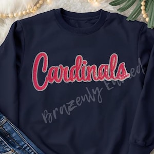 May include: Navy blue sweatshirt with the word "Cardinals" in red script with a silver outline. The text "Brazenly Edited" is written in a cursive font below the word "Cardinals".