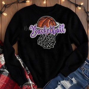 May include: Black crew neck sweater with a basketball graphic. The graphic features an orange basketball above a purple "Basketball" script and a white net. The sweater is made of a soft material.