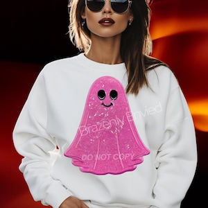 May include: White sweatshirt featuring a pink glittery ghost graphic with a smiling face. The text "Brazenly Envied" and "DO NOT COPY" are printed on the sweatshirt. The background is a gradient of red and black.